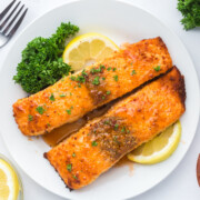Two pieces of hot honey salmon recipe on a plate with parsley and lemon