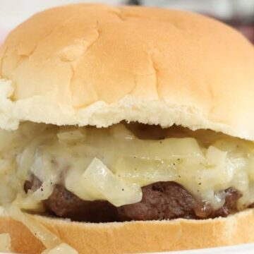 A hamburger with melted cheese and sautéed onions on a soft bun, served on a white plate.