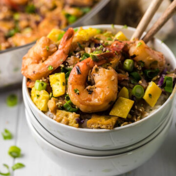 Bowl of shrimp and vegetable stir-fry over rice with chopsticks, garnished with green onions on a wooden table. Explore more about shrimp nutrition in our latest section.