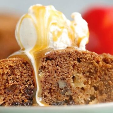 A slice of sticky toffee apple pudding with vanilla ice cream on top, drizzled with caramel sauce, on a plate.