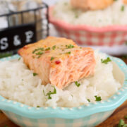 A piece of baked salmon with mayo over a bowl of rice.