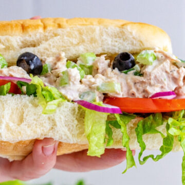 Person holding a Tuna Salad Sandwich with olives, lettuce, tomato's and tuna