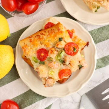 A plate with two pieces of salmon pizza on it and bowls of ingredients to the side.