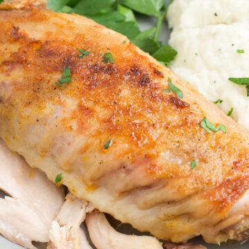 A turkey wing on a plate with mashed potatoes and broccoli.