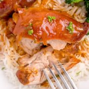 A fork cutting into a piece of crockpot apricot chicken over rice on a plate.