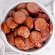 A white bowl filled with slices of cooked kielbasa on a marble surface showcases an easy recipe perfect for the air fryer.