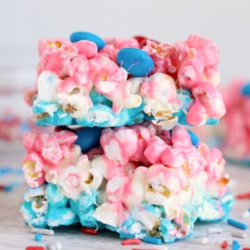 Two bars of pink, blue, and white popcorn treats with blue candy-coated chocolates on a light surface, surrounded by red, white, and blue sprinkles—a perfect addition to your Red-White-Blue Desserts collection.