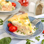 A slice of salmon quiche on a plate with a fork and some tomatoes on the side.