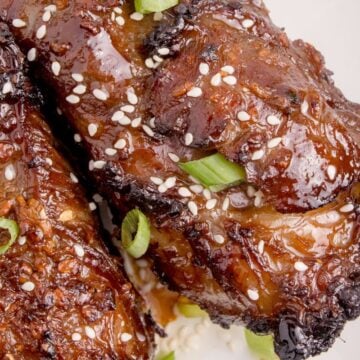 Short ribs garnished with sesame seeds and chopped green onions on a plate.