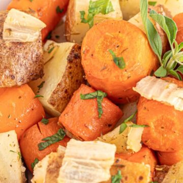 A close-up view of a dish featuring roasted carrots, potatoes, and onions garnished with fresh herbs serves as the perfect spotlight for any meal.