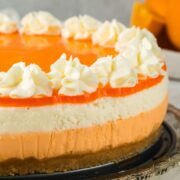 Orange creamsicle cheesecake with different colored layers and white swirls of whipped cream on top.