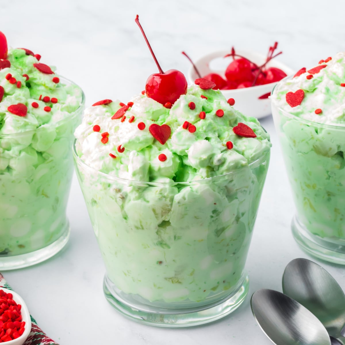 Cup of green Pistachio Fluff salad with red sprinkles and a cherry on top 