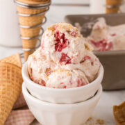 A bowl of strawberry crunch ice cream with small pieces of rolled waffle cones placed next to it.
