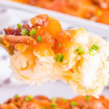 A fork holding bite of cheesy potato casserole, garnished with chopped green onions and bits of bacon – the perfect addition to your side dishes spread.