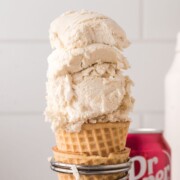 Two heaping scoops of Dr. Pepper ice cream in a cone being held up by a wire stand.
