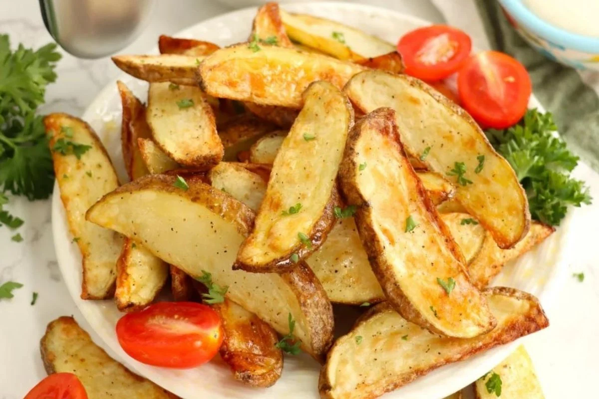 A plate of seasoned potato wedges garnished with parsley, accompanied by fresh cherry tomatoes on the side.