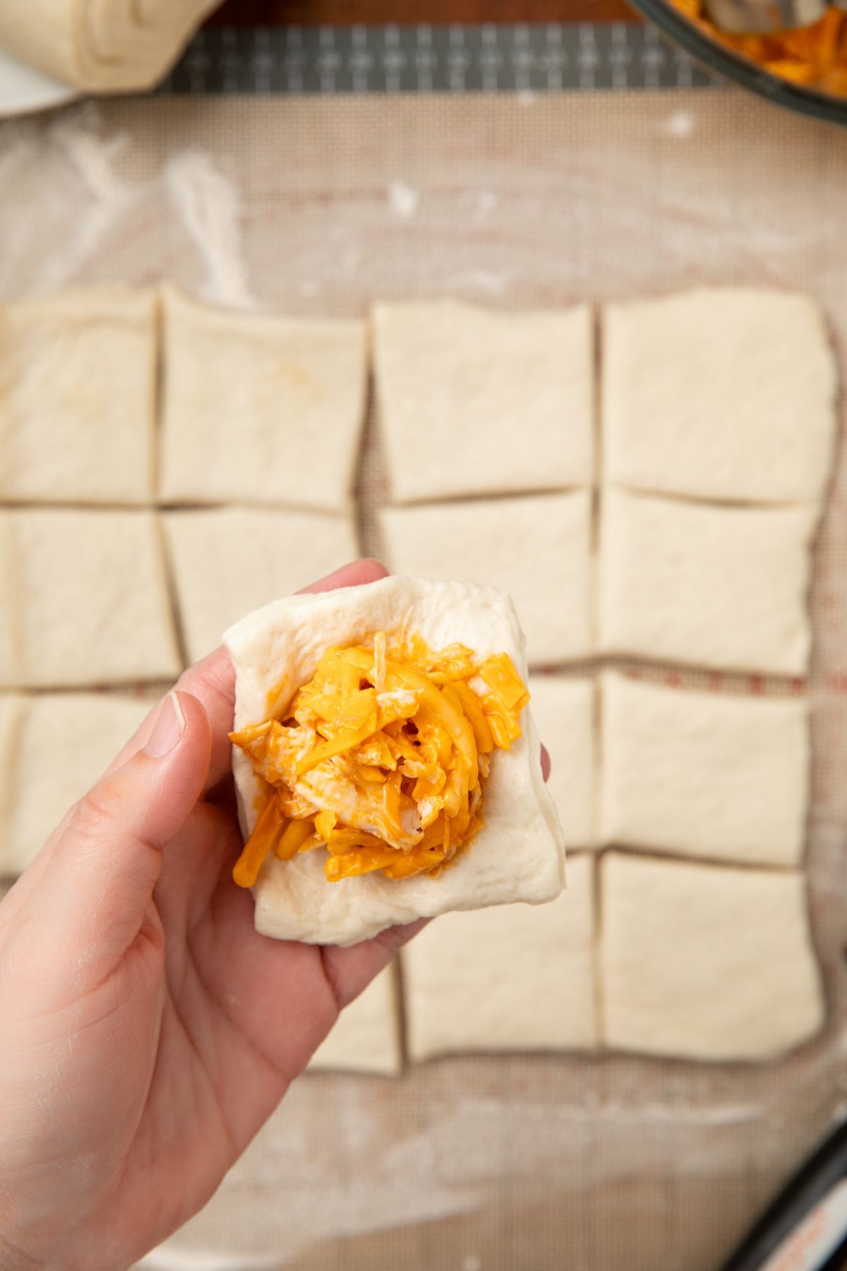 The chicken mixture place on the pizza dough and a hand holding it up over more dough below.
