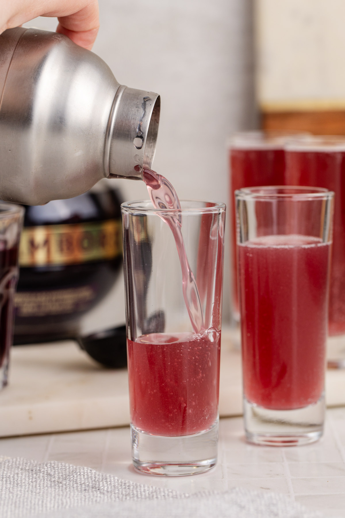 Shaker pouring drink into shot glass.