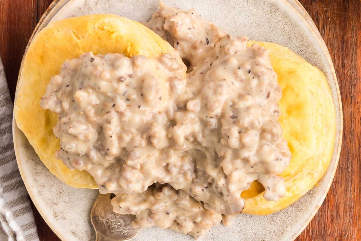 A biscuit cut in half covered in gravy on a plate.