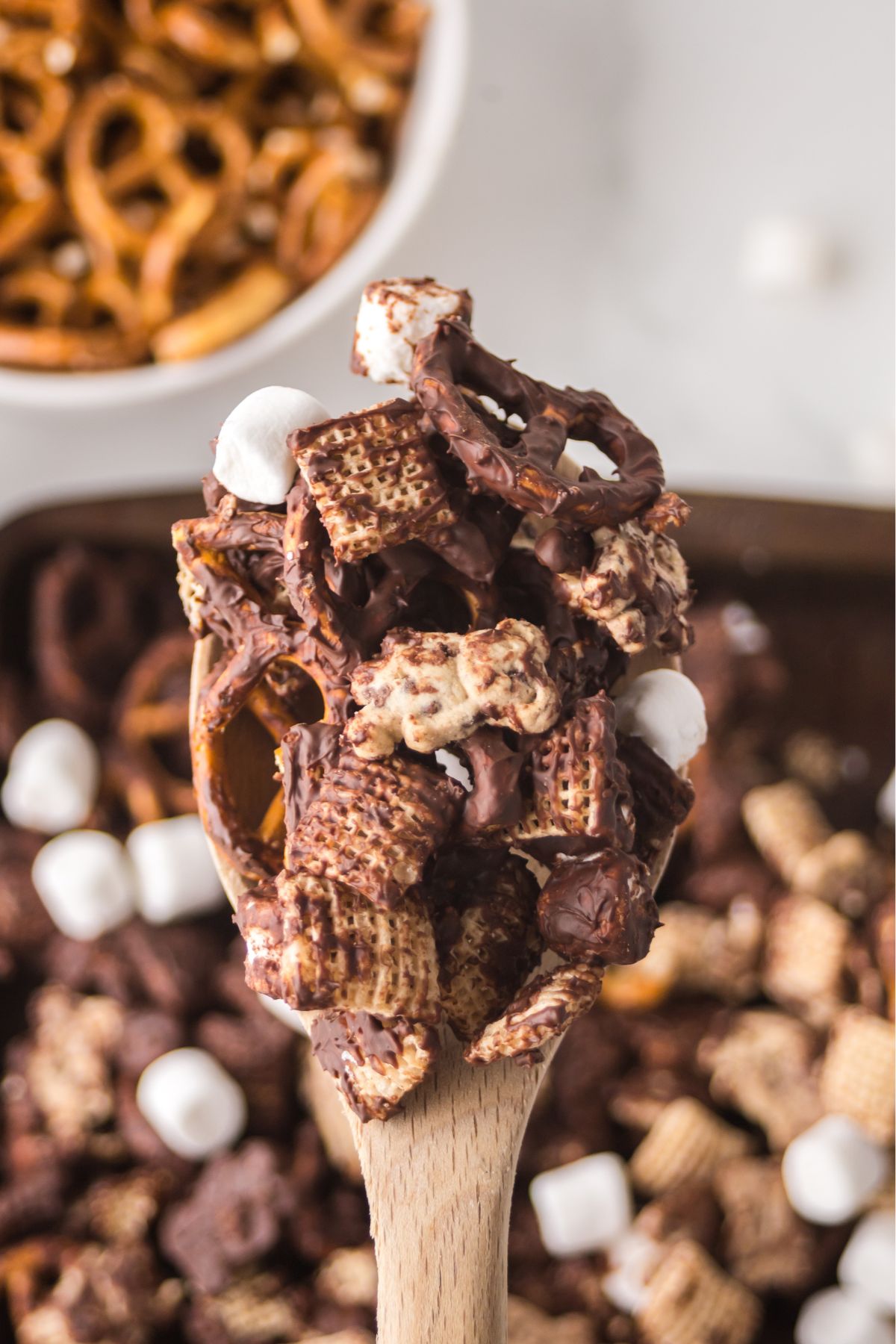 A wooden spoon held in the air full of snack mix.