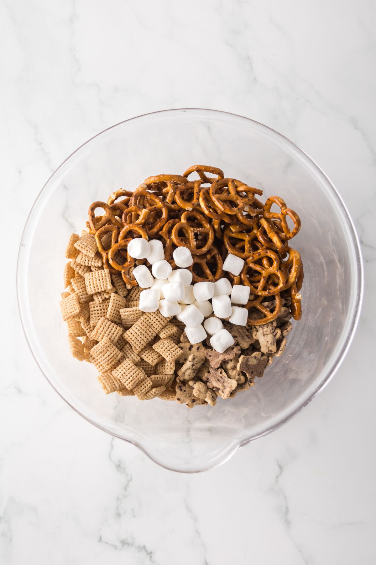 A bowl full of teddy grahams, marshmallows, chex and pretzels.