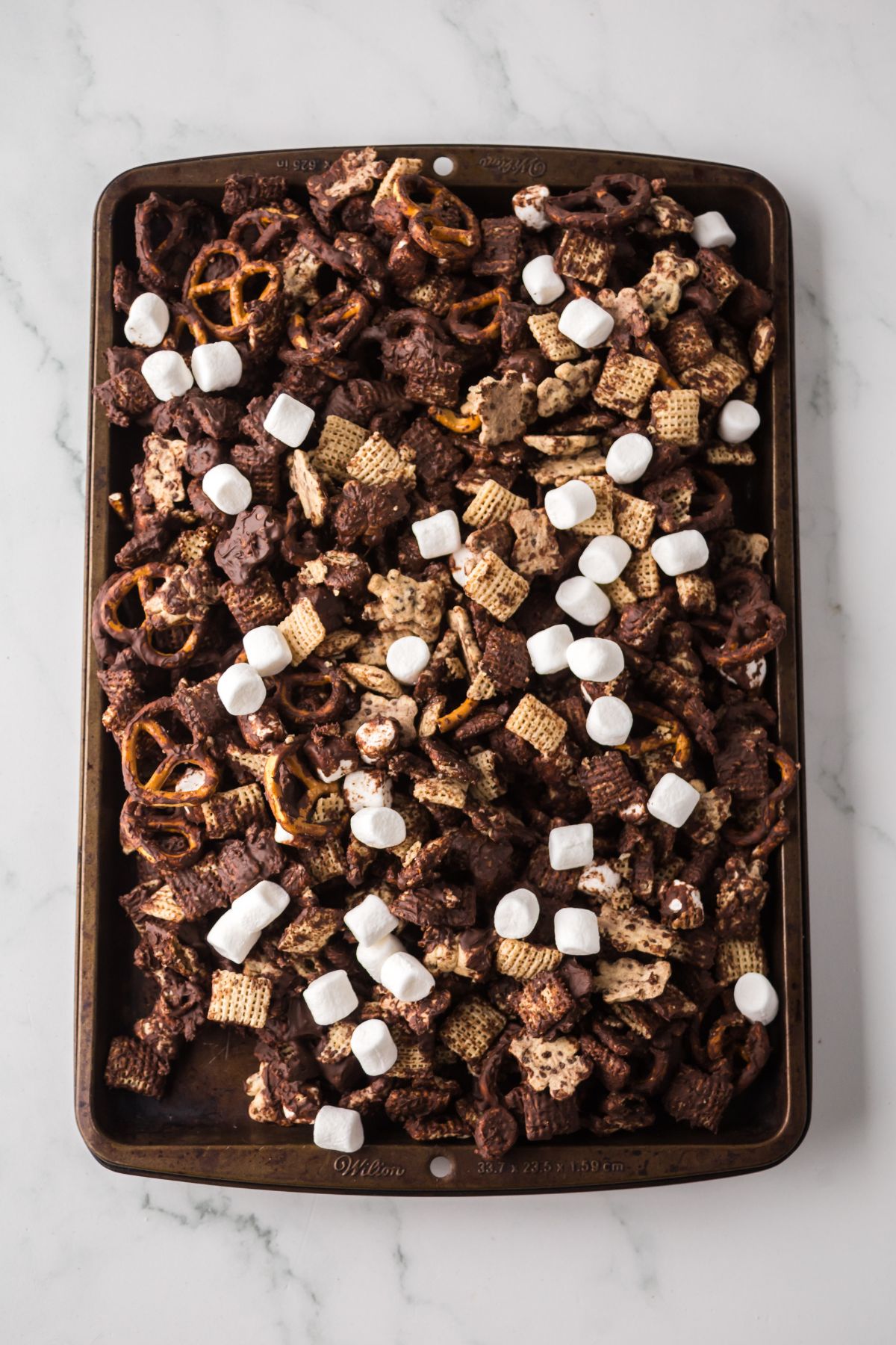 Snack mix covered in chocolate setting on rimmed bking sheet.