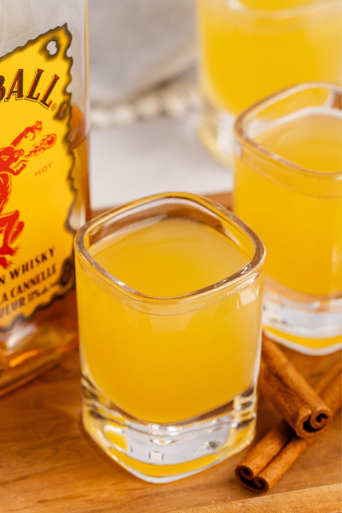 Two shots on serving tray with bottle of whiskey and cinnamon sticks.