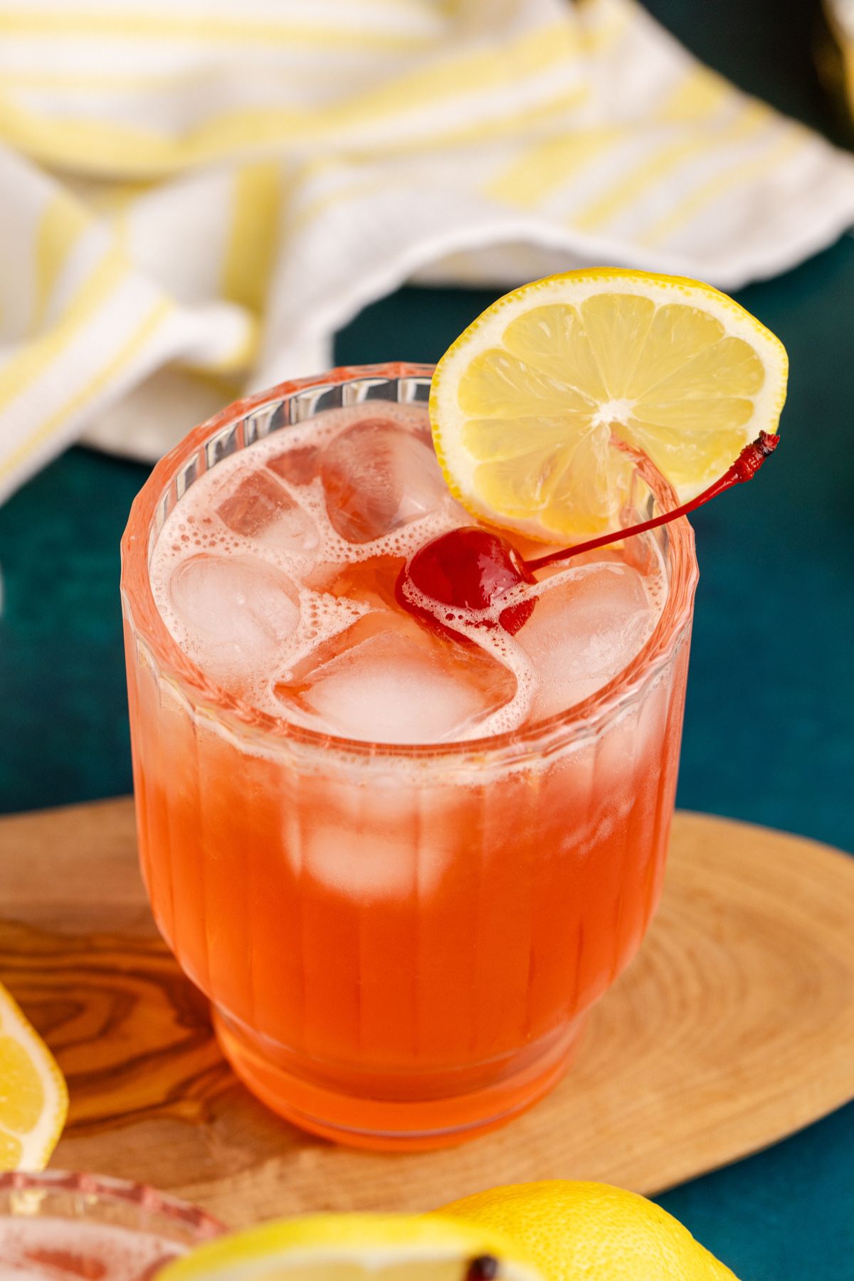 cocktail garnished with cherry and lemon slice on cutting board.