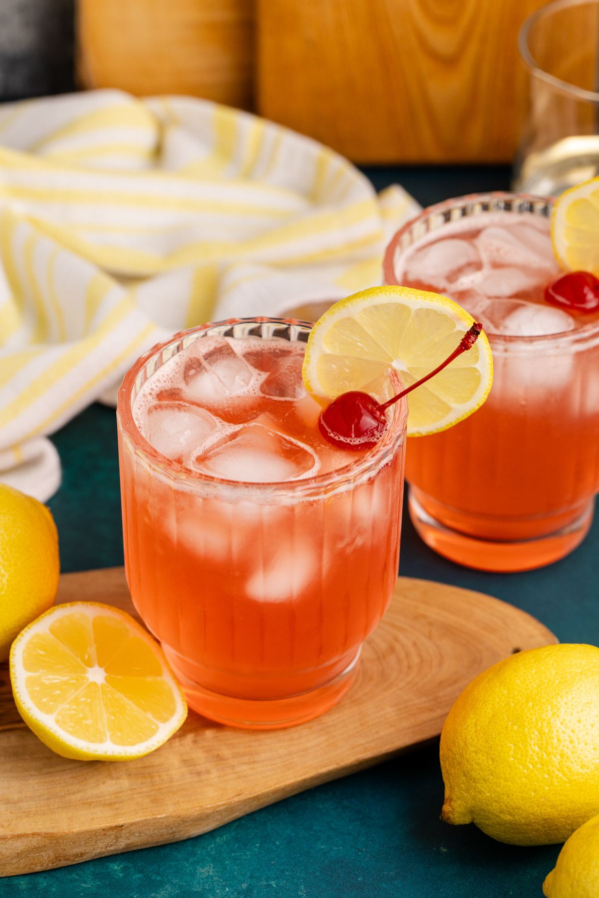 masters azalea cocktail garnished with lemon and cherry on cutting board.