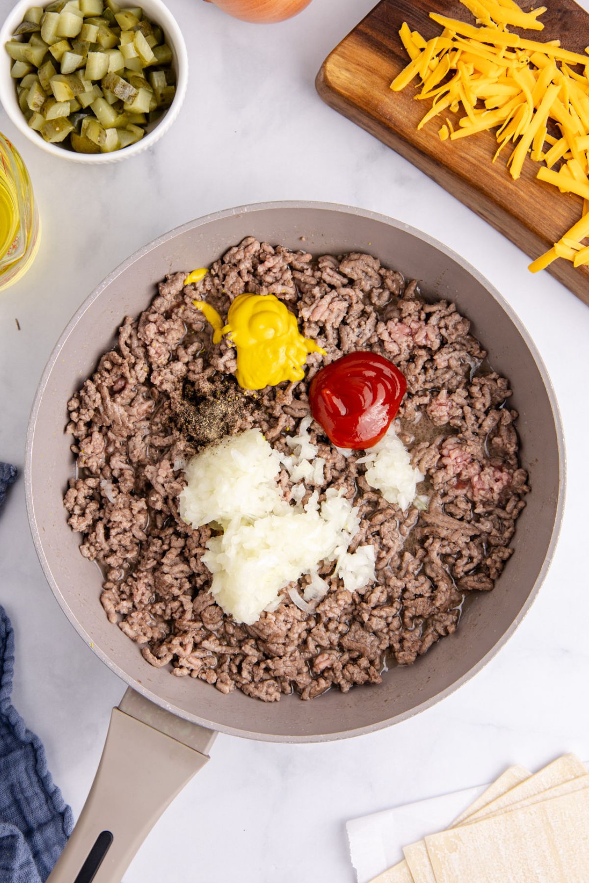 Ground beef, onion, ketchup, mustard, and pepper cooking in a skillet.