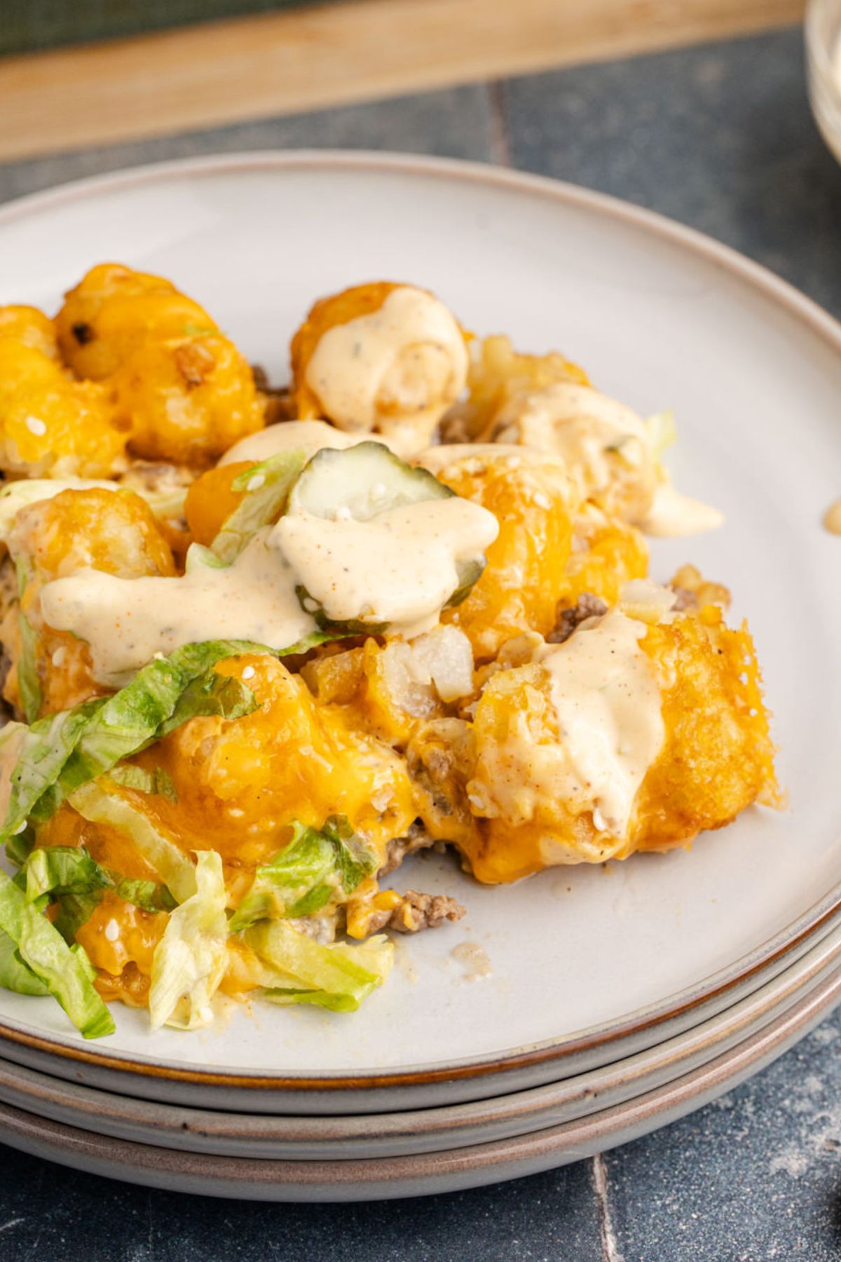 Tater tots with beef and cheese topped with pickles, lettuce and sauce on a plate.
