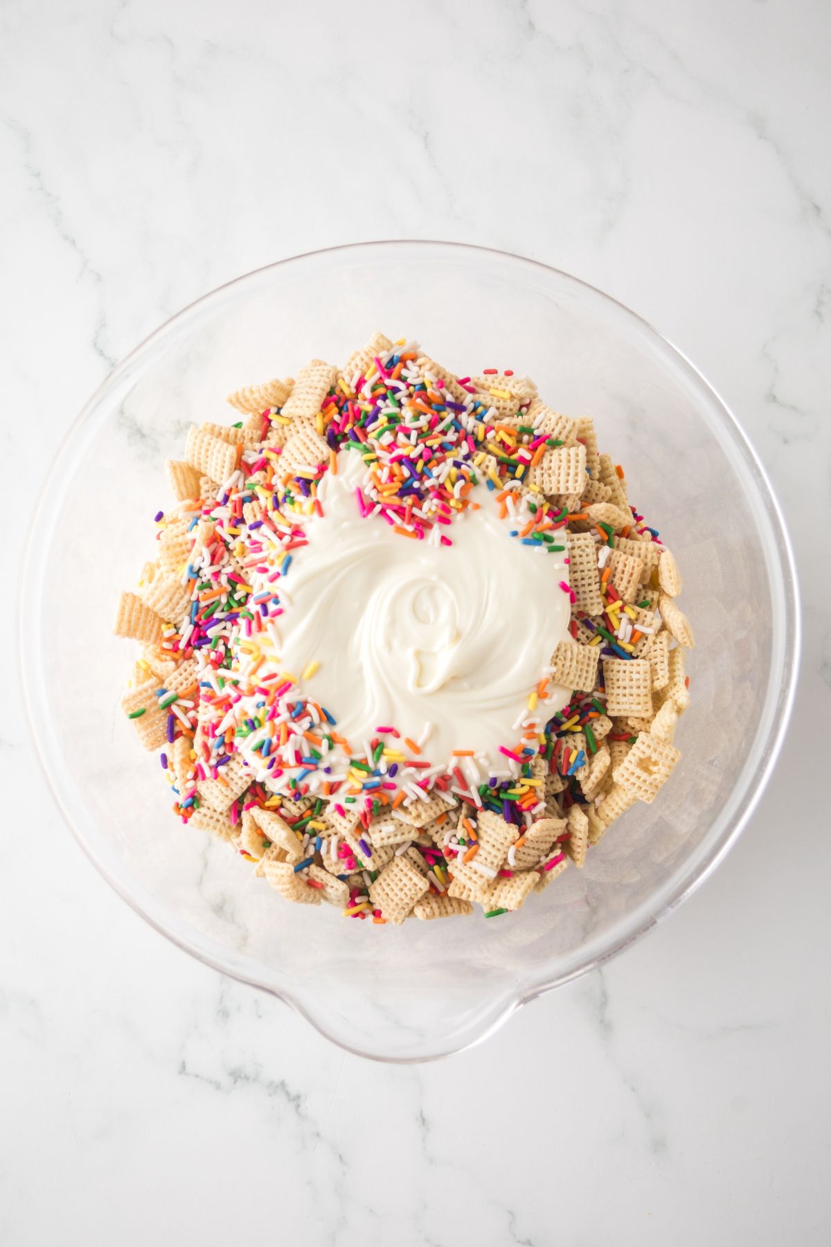 A large bowl full of chex mix, melted chocolate and sprinkles ready to be blended.