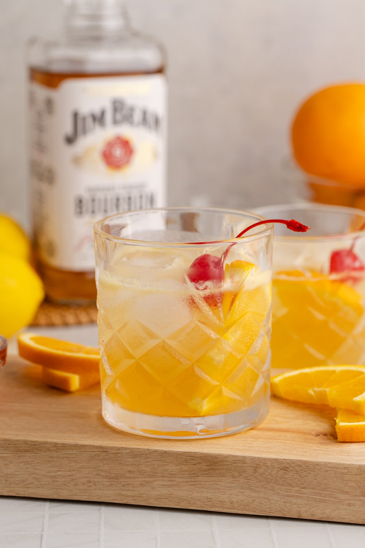Cocktails served with a cherry garnish on a cutting board.