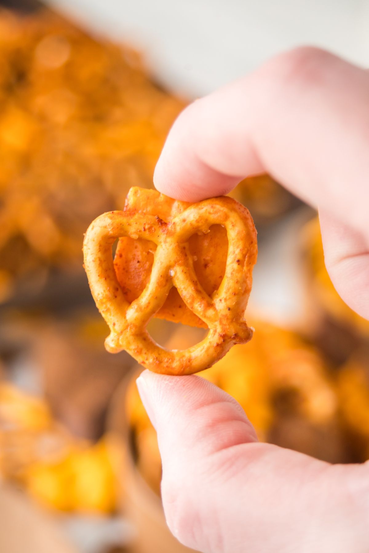 A hand holding a pretzel stuck to a cheesz-it in the air.