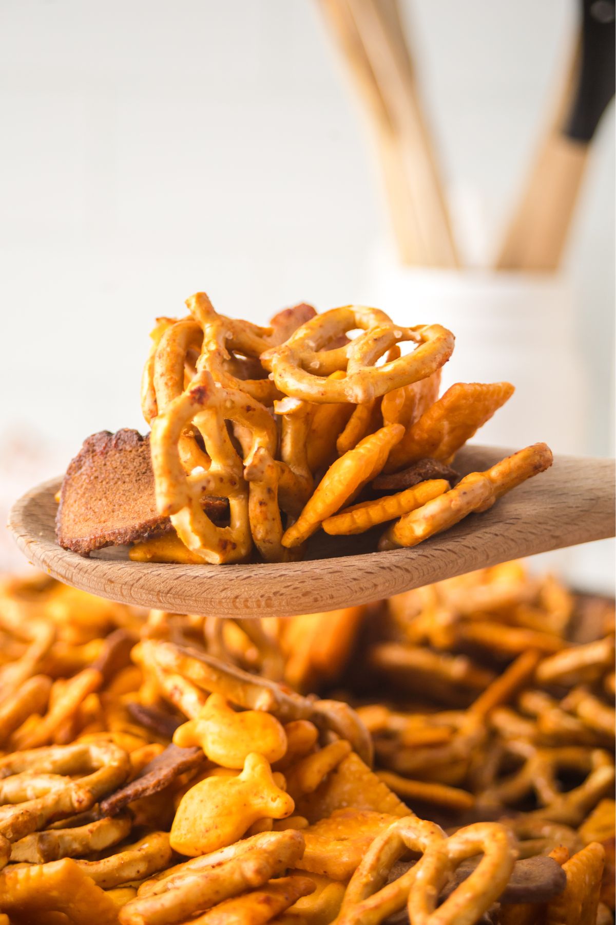 A wooden spoon full of snack mix held above a bowl.