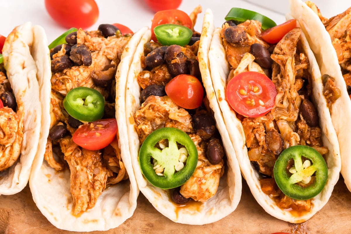 A row of tacos on cutting board.