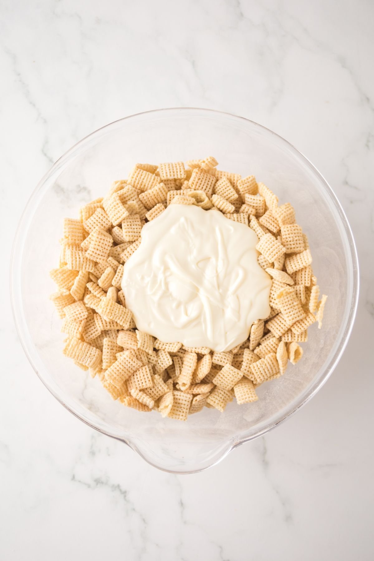 Chex mix in a large bowl covered in melted chocolate with lemon juice ready to be blended.