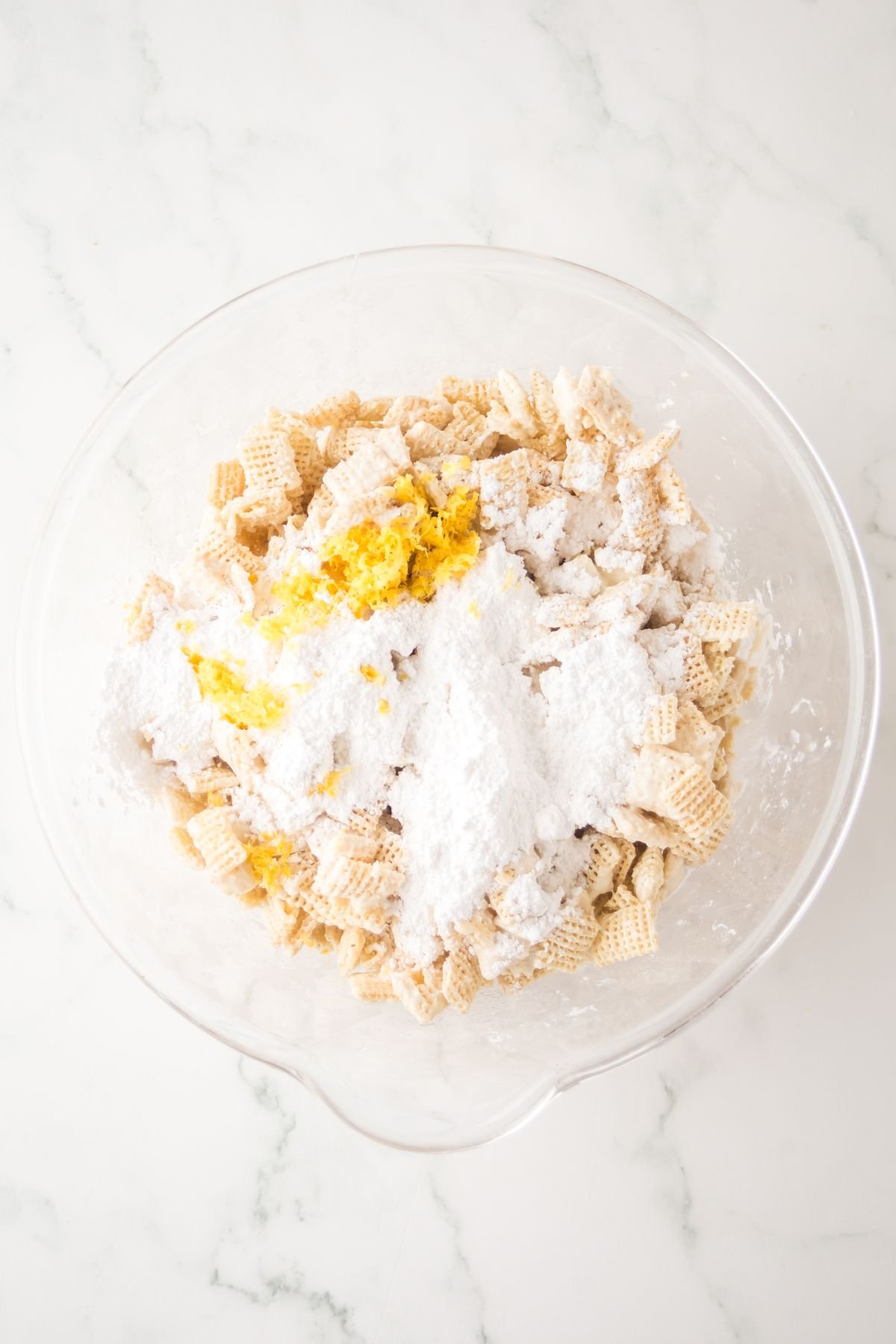 Bowl of chex mix with lemon zest and powdered sgar ready to be folded together.