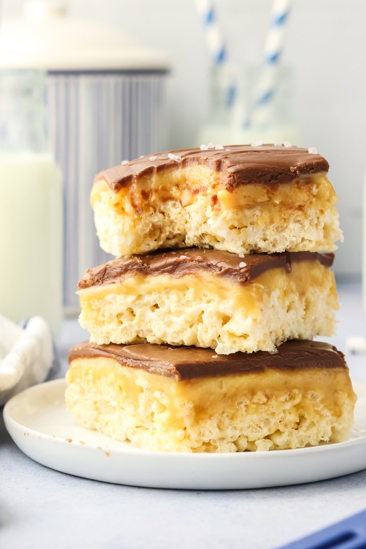 Rice krispie treats with caramel and chocolate on top, stacked on a plate.
