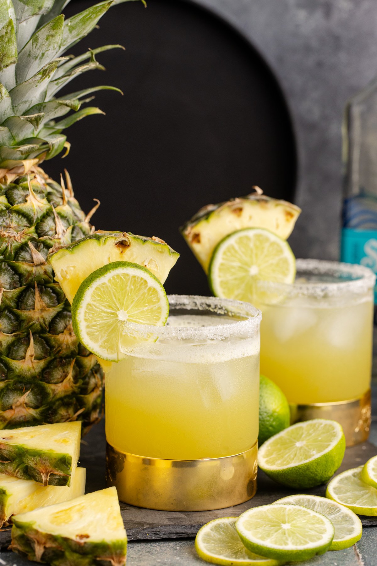 Two pineapple margarita cocktails garnished with a pineapple and lime slice.