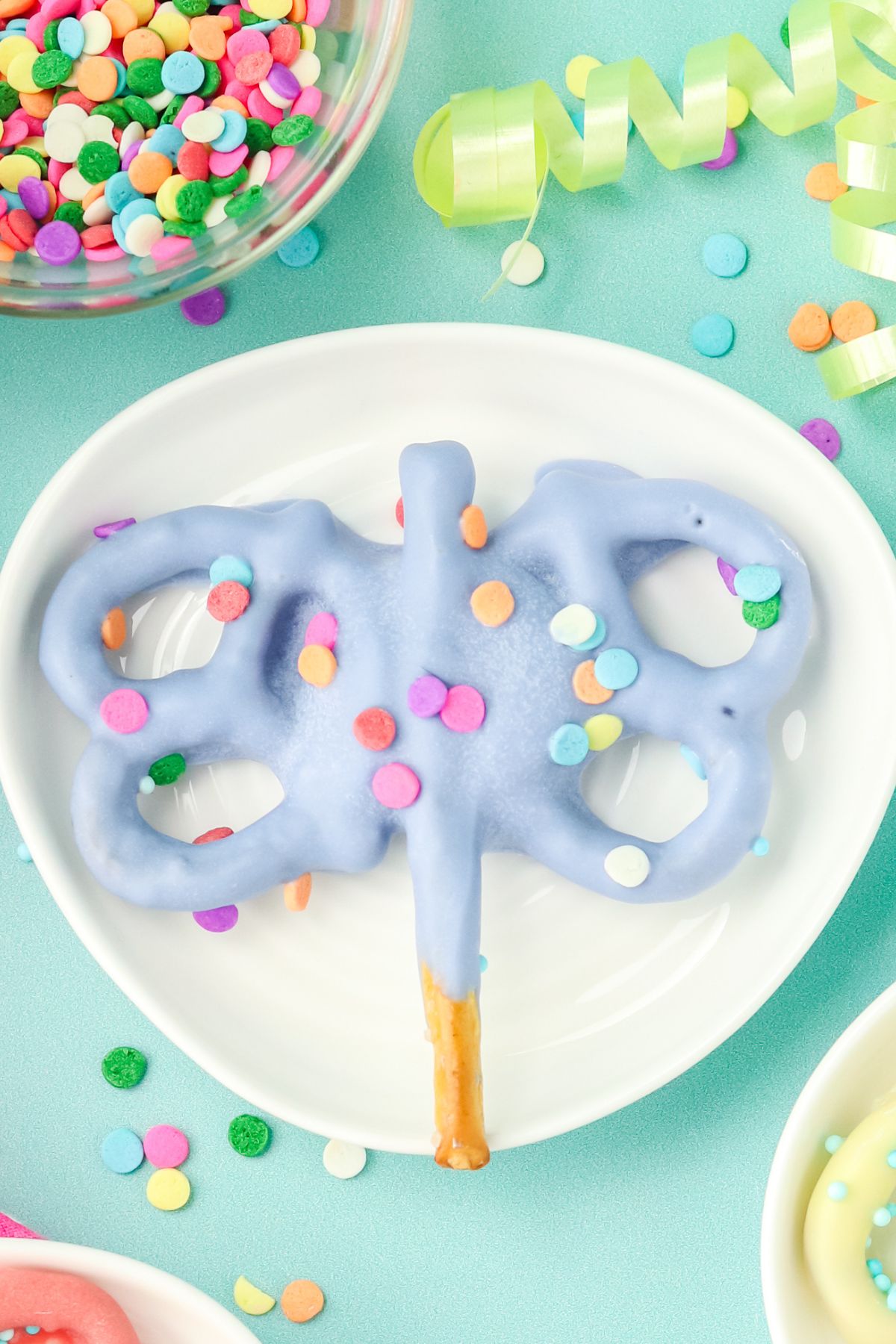 Purple pretzel butterfly with sprinkles on a white plate.