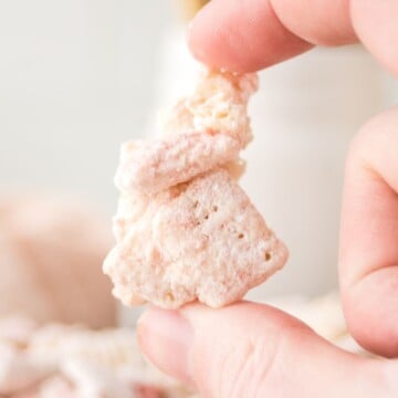 A bite of strawberry muddy buddie held in the air between two fingers.