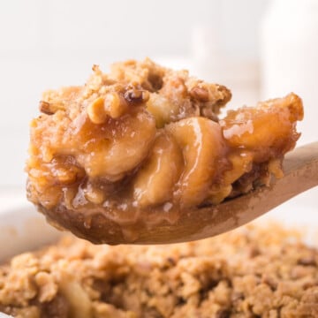 A wooden spoon holding up a helping of banana cobbler over the dish of more.