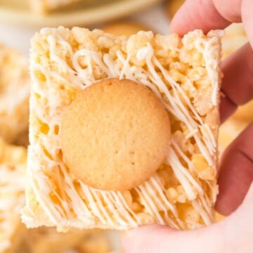 Banana pudding rice krispie treats held up by a hand over a plate of more.