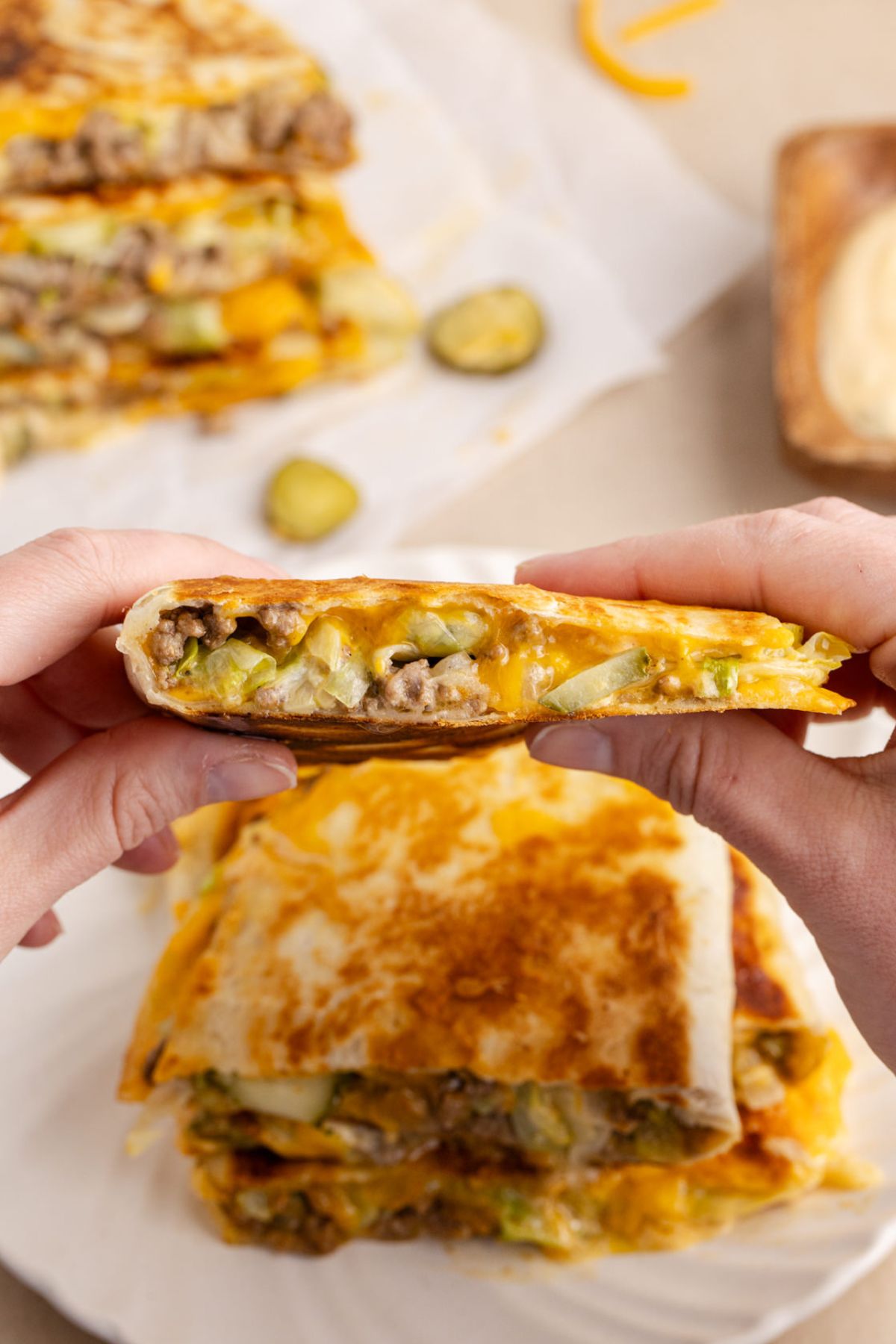 A Big Mac quesadilla held up in the air to eat over a plate of more.