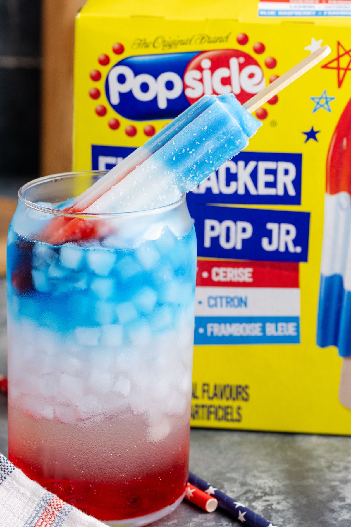 A popsicle leaning in drink with popsicle box behind.