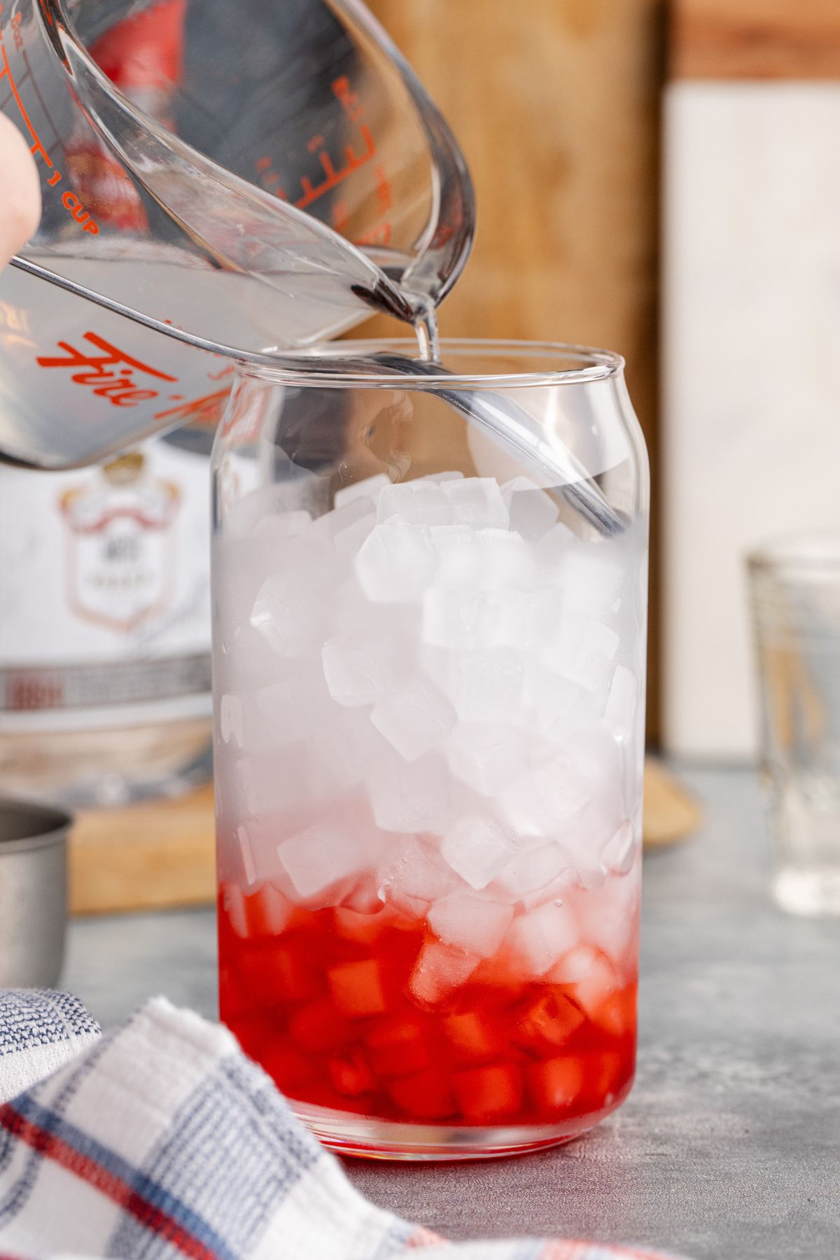Lemonade and vodka in measuring cup being poured on top of spoon.