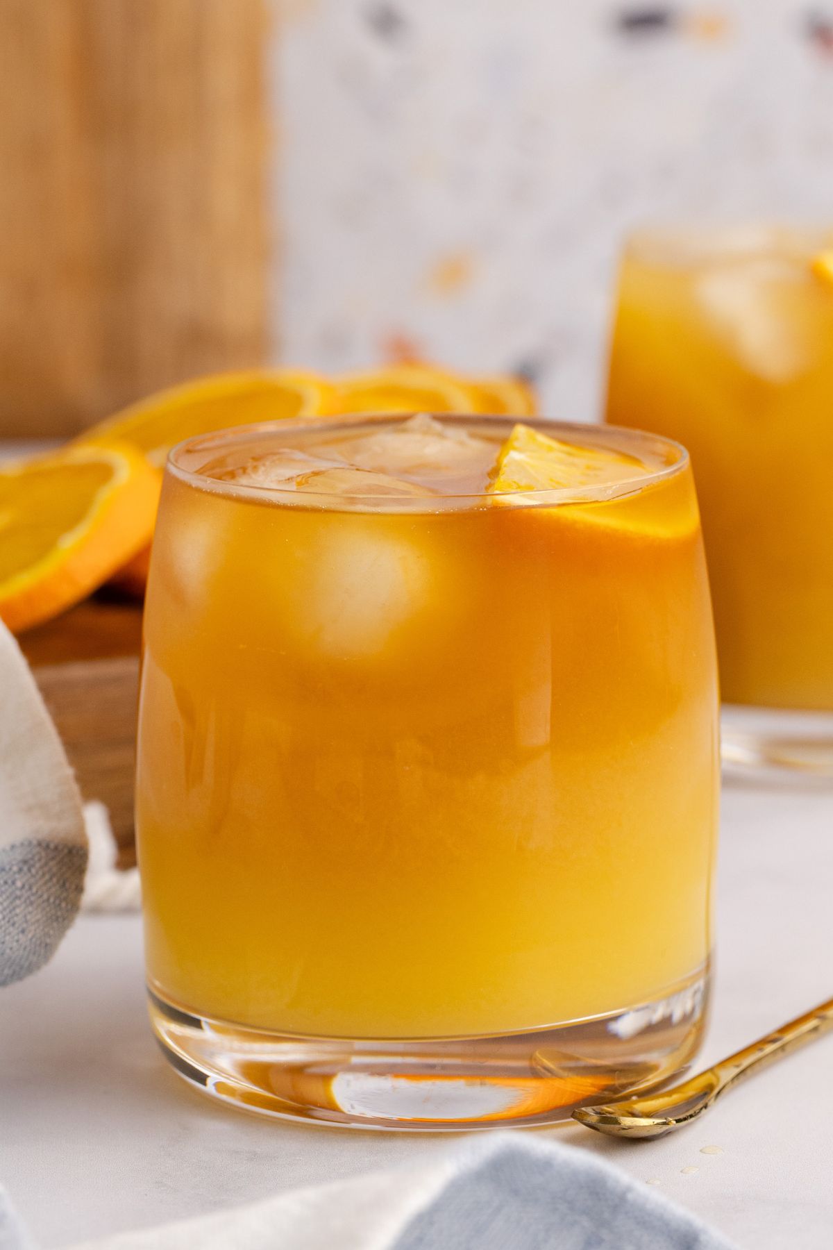 Made cocktail garnished with an orange slice on a table with another drink in the background.