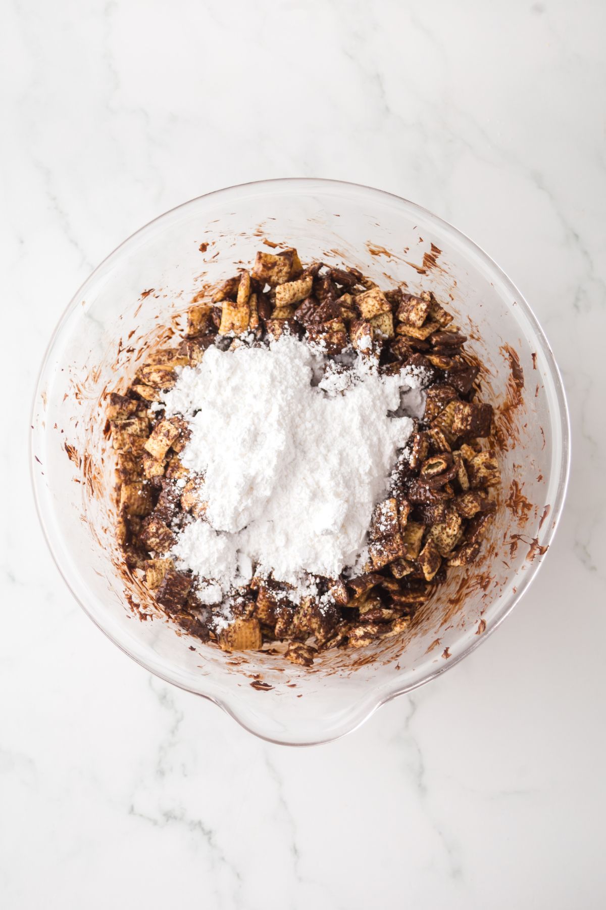 Powdered sugar added to bowl to cover coated chex cereal.
