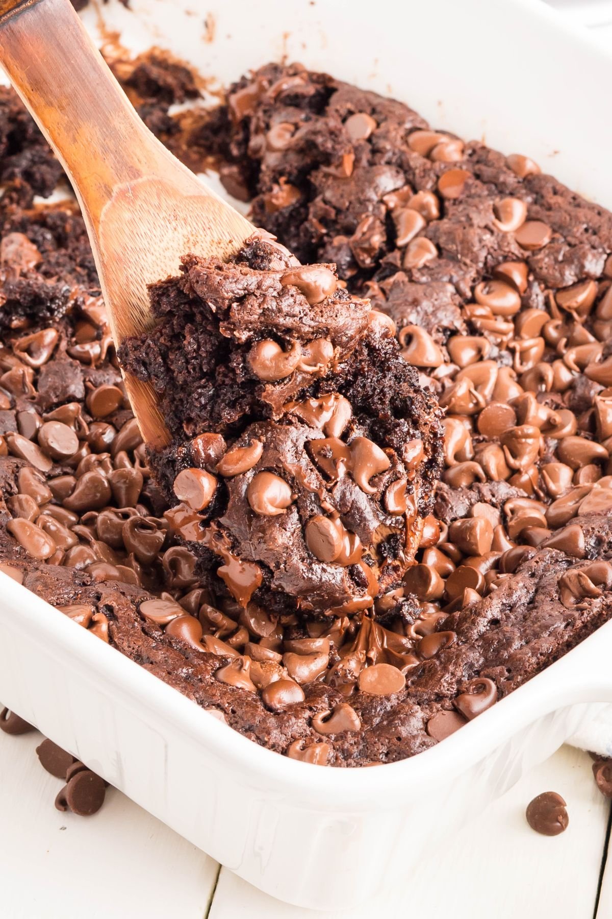 Chocolate pudding cake with chocolate chips on top, with some cake being scooped out with a wooden spoon.